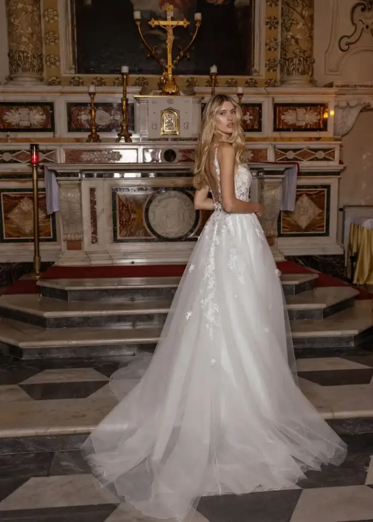 A woman in a white lace wedding gown stands in front of an ornate altar with a crucifix, exuding elegance and solemnity in a richly decorated church.