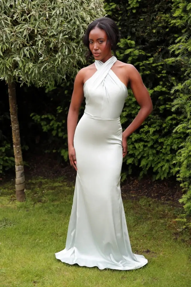 A sleek halterneck gown in liquid satin with a tied bow and open-back detail, designed to glide effortlessly from aisle to dance floor.