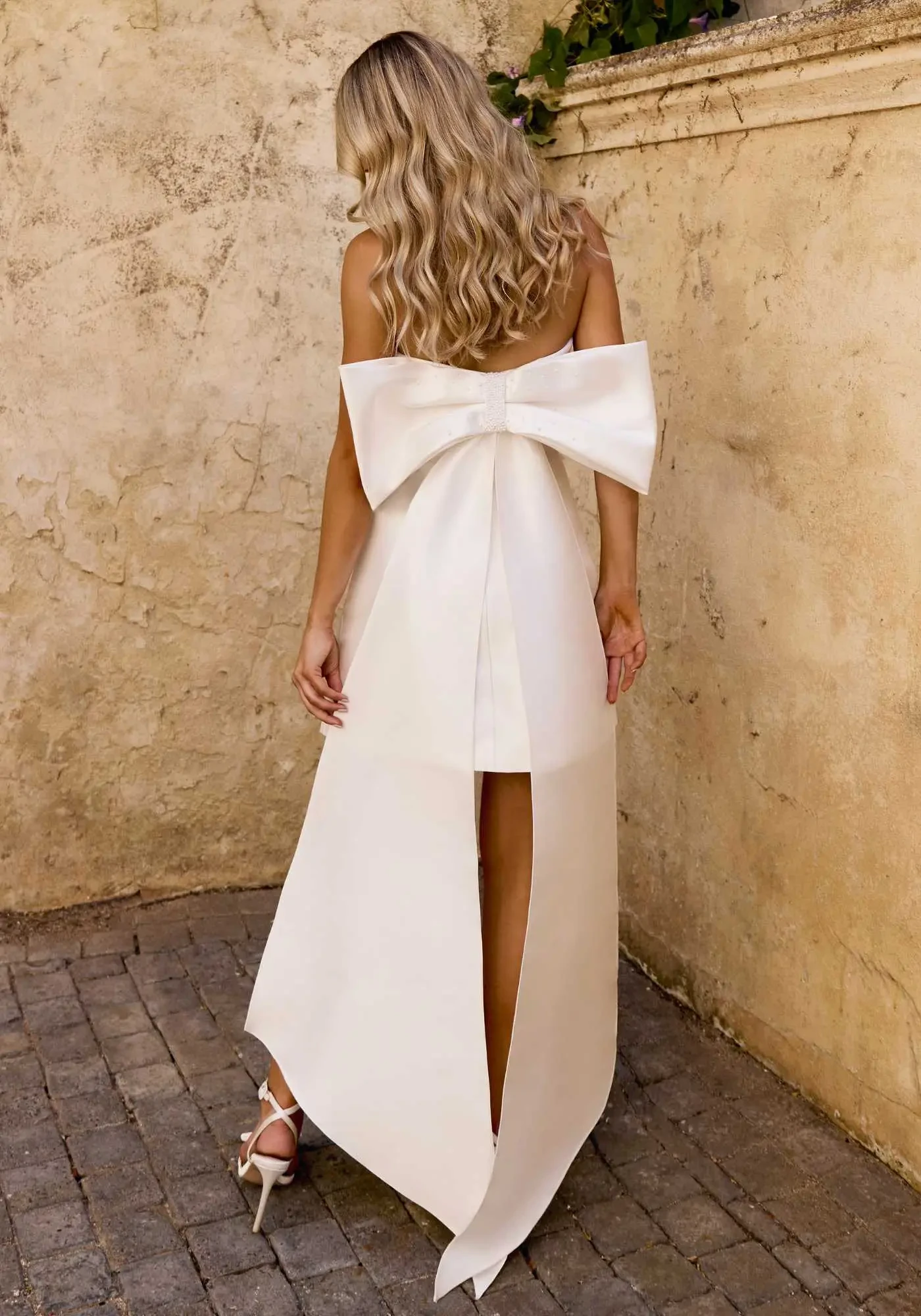 Model is wearing a mikado mini with elongating seam lines, a cuffed neckline, and a detachable oversized beaded bow for a modern statement.