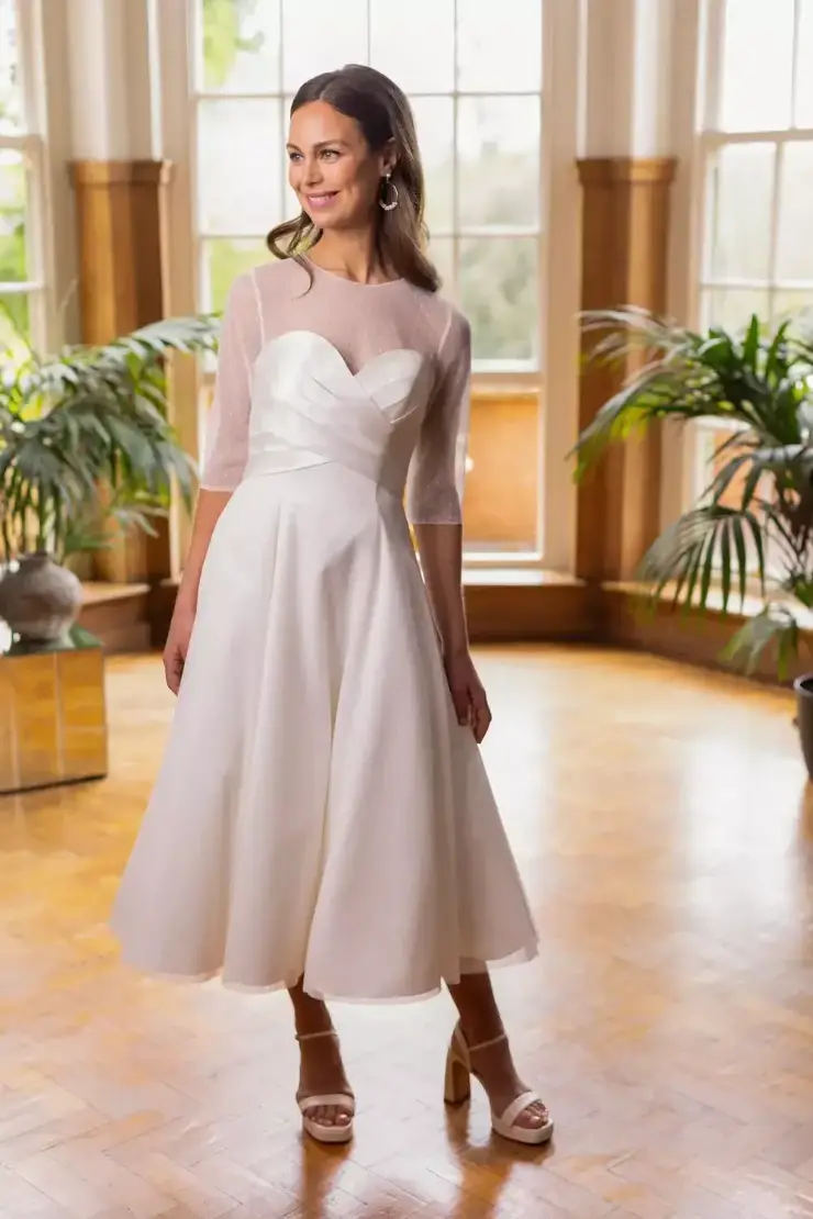 Model is wearing a satin tea-length gown with a sweetheart bodice, crossover pleating, and a detachable polka dot bolero for two chic looks in one.